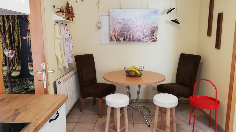 A cozy dining area with a round table and two chairs. In the background, a decorative picture of a flower meadow hangs.