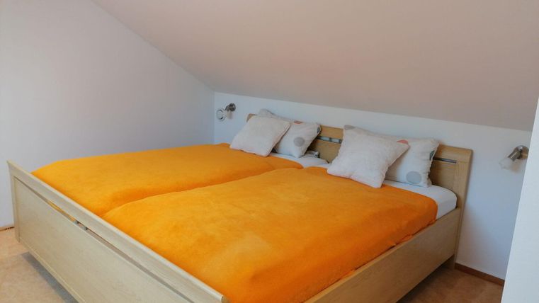 A cozy bedroom with a large, bright bed and orange blankets. The walls are white and create a calm atmosphere.
