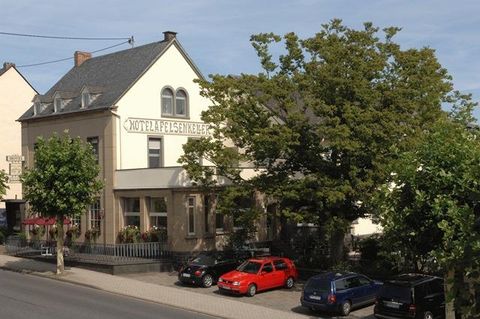 Ein Gebäude mit der Aufschrift „Motel Felsenblick“ steht in einer ruhigen Umgebung. Vor dem Motel parken mehrere Autos und Bäume umgeben die Fassade.