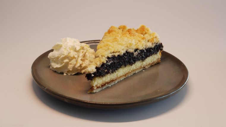Ein Stück Kuchen auf einem Teller, mit einer Schicht aus dunkler Füllung und Sahne. Der Kuchen hat eine goldene, krümelige Oberseite.