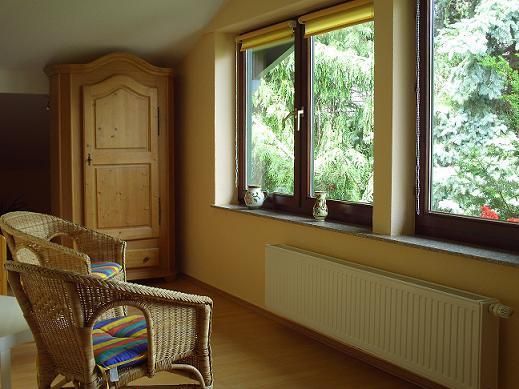 A bright room with two cozy chairs and a large window. Outside, green trees are visible.