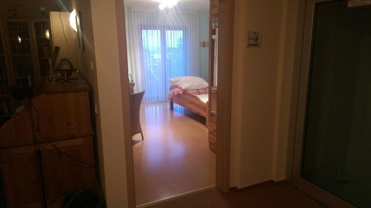 A wide hallway with a view of a bedroom. The room has a bed and large windows that let in light.