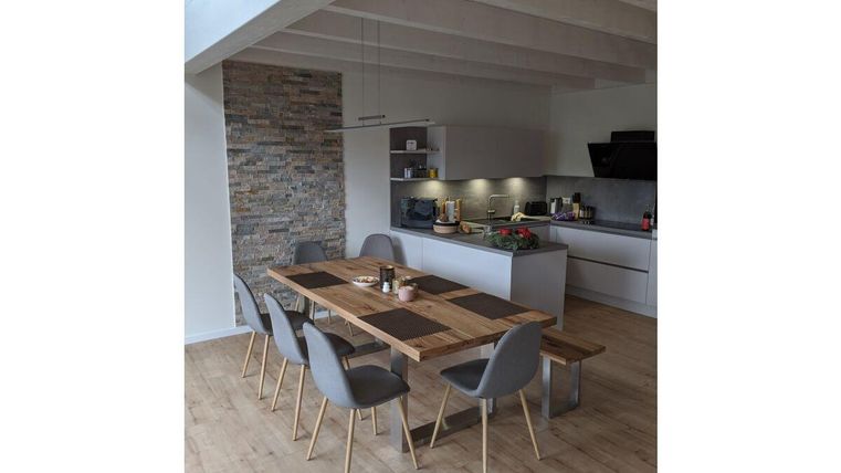 Ein moderner Essbereich mit einem langen Holztisch und grauen Stühlen. Die offene Küche hat eine helle, einladende Atmosphäre.