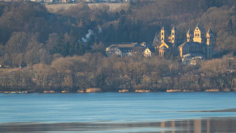 A picturesque landscape with a tranquil lake and a historic church in the background. The trees and the gently rolling hills create a peaceful atmosphere.