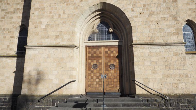 The entrance door of a church made of wood is clearly visible. The entrance is surrounded by a stone wall and has a large arch shape.