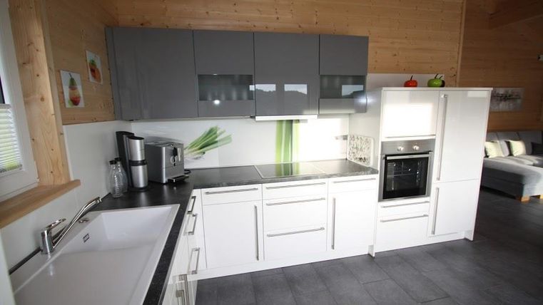 Eine moderne Küche mit einer weißen Arbeitsfläche und grauen Oberschränken. Die Wände sind aus Holz und es gibt viel natürliches Licht.
