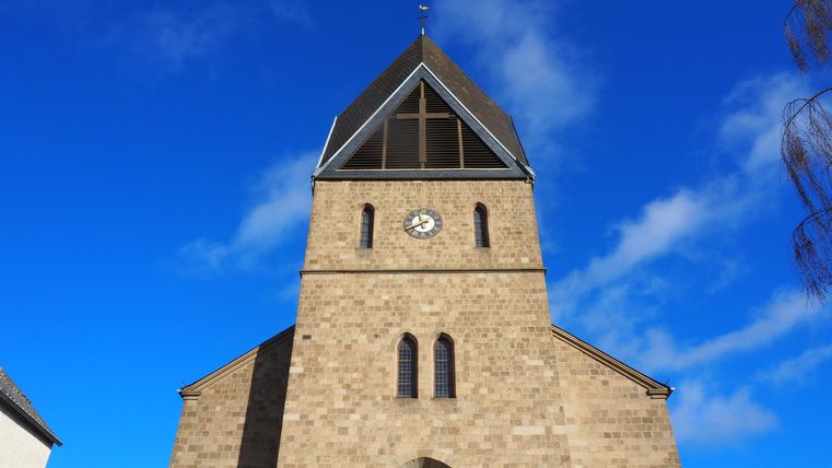 A stone church with a distinctive tower and a clock face. The sky is clear and blue.