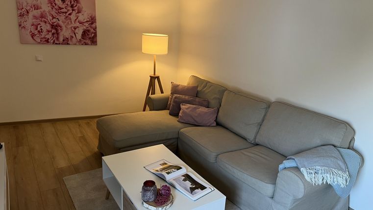 Ein gemütliches Wohnzimmer mit einem beigen Sofa und bunten Kissen. Eine Stehlampe und ein Couchtisch sorgen für eine einladende Atmosphäre.