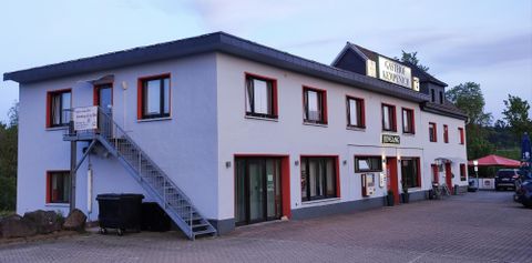 A modern building with several windows and an entrance. Outside, there is a staircase and some parking spaces.
