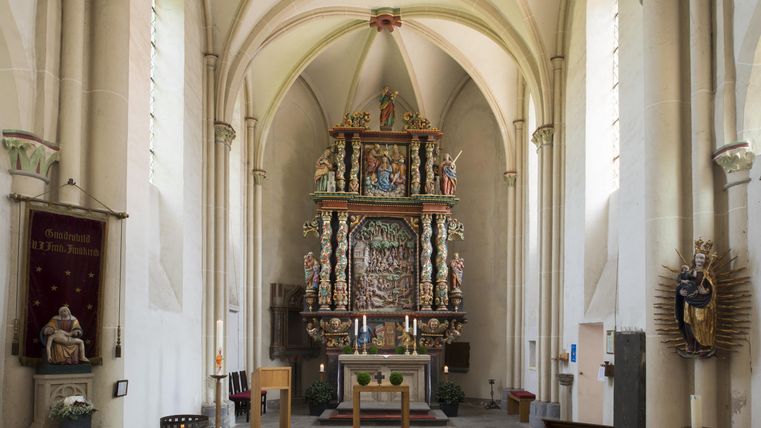 Ein schöner Kircheninnenraum mit einer kunstvoll gestalteten Altaranlage. Die bunten Figuren und das hohe Gewölbe verleihen dem Raum eine besondere Atmosphäre.