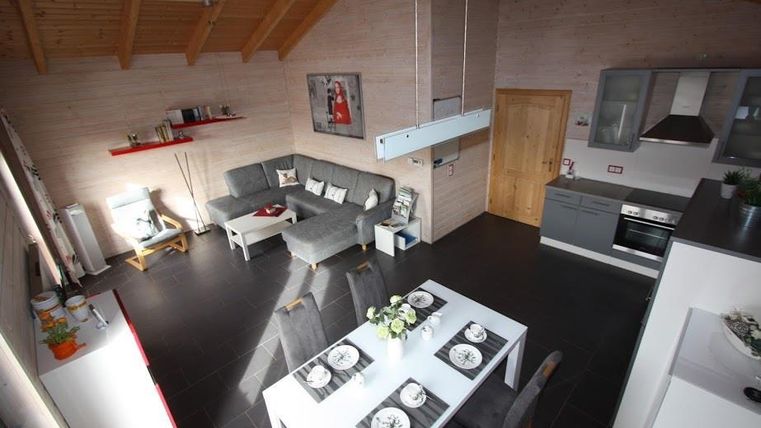 Eine moderne, helle Wohnung mit offener Wohnküche und einem großen Esstisch. Die Holzbalkendecke und die eleganten Möbel verleihen dem Raum eine gemütliche Atmosphäre.