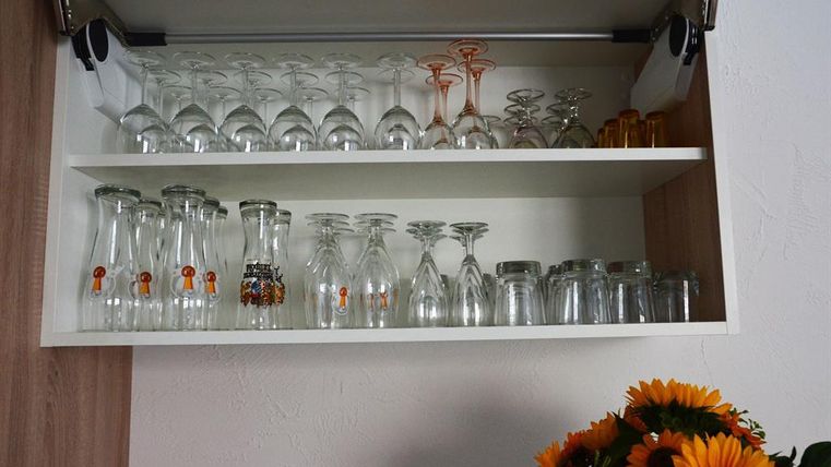 Ein Küchenschrank mit mehreren Regalen, gefüllt mit verschiedenen Gläsern. Darunter befinden sich klare Gläser, Weingläser und dekorative Flaschen.