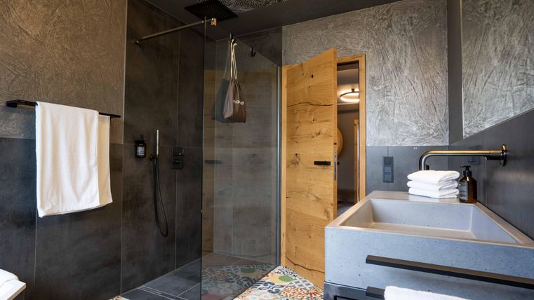 Ein modernes Badezimmer mit einem gläsernen Duschbereich und einem stilvollen Waschbecken. Der farbenfrohe Boden und die Holzdetails sorgen für eine einladende Atmosphäre.