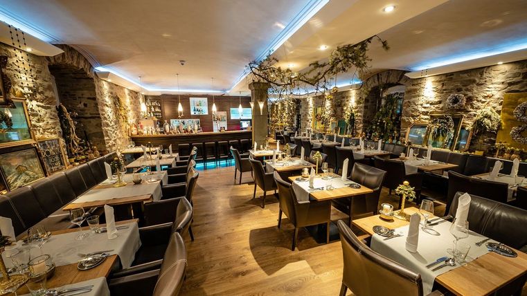 A cozy restaurant with wooden floors and stone walls. Tables are elegantly set and the lighting creates an inviting atmosphere.