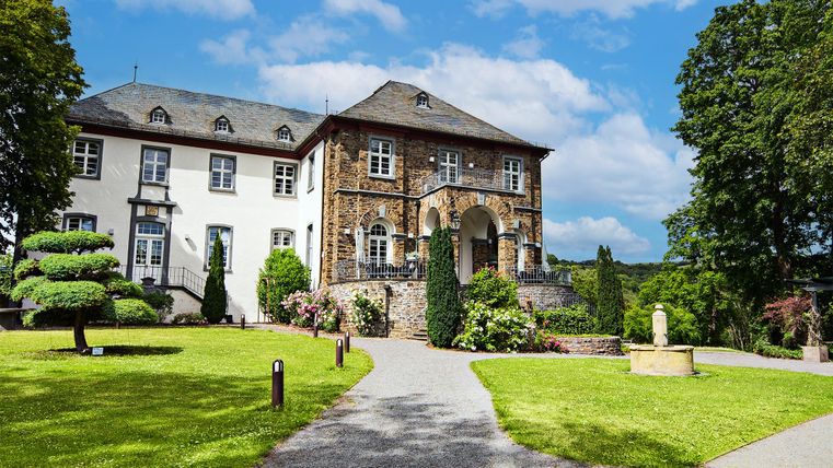 Ein beeindruckendes Gebäude mit historischer Architektur und einem gepflegten Garten. Umgeben von Bäumen und einem blauen Himmel strahlt es Ruhe und Eleganz aus.