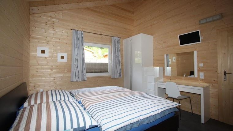 Ein gemütliches Schlafzimmer mit Holzverkleidung und einem großen Doppelbett. Es gibt einen Schreibtisch, einen Stuhl und ein Fenster mit Vorhängen.