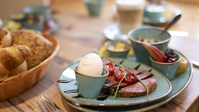 A beautifully set table with a plate displaying beef, fresh vegetables, and a decorated egg. In addition, there are various side dishes in small bowls and a basket with rolls.