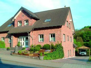 Ein modernes, rotes Ziegelhaus mit einem Satteldach. Der Garten ist gepflegt und es gibt eine Auffahrt für Autos.