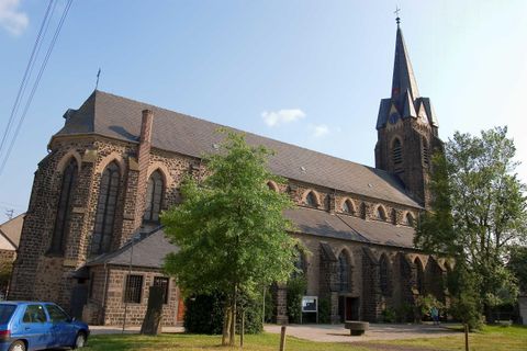 Eine imposante Kirche mit einem hohen Turm. Umgeben von Bäumen und einem klaren Himmel.