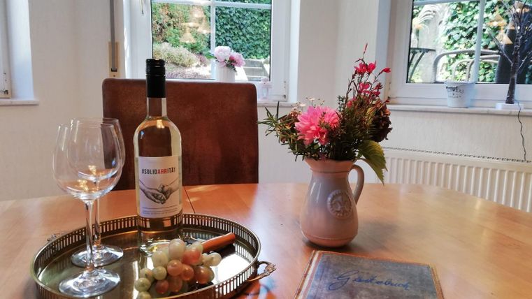 A lovingly set table with a glass of wine and fresh grapes. In addition, a bouquet of flowers in a vase and an open book.
