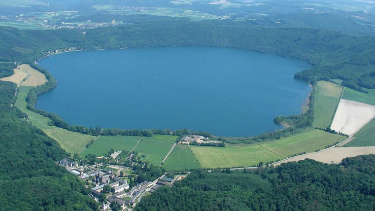 Ein schöner See umgeben von grünen Wäldern und Feldern. Die Landschaft ist friedlich und naturbelassen.