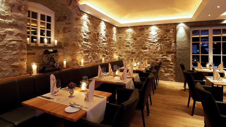 A cozy restaurant with stone walls and soft lighting. The tables are elegantly set, creating an inviting atmosphere.