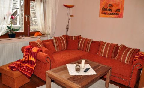 Ein gemütliches Wohnzimmer mit einem orangefarbenen Sofa und bunten Kissen. Auf dem Couchtisch steht eine Kerze und ein kleiner Dekorationsgegenstand.