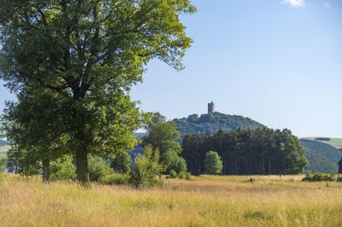 Eine idyllische Landschaft mit einem großen See und umgebenden Wäldern. Im Vordergrund sind Felder und ein Gebäude sichtbar.