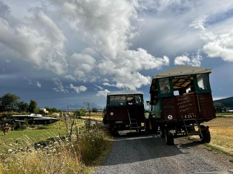 Zwei fahrende Wohnmobile stehen auf einem Schotterweg. Im Hintergrund sind Felder und ein bewölkter Himmel zu sehen.