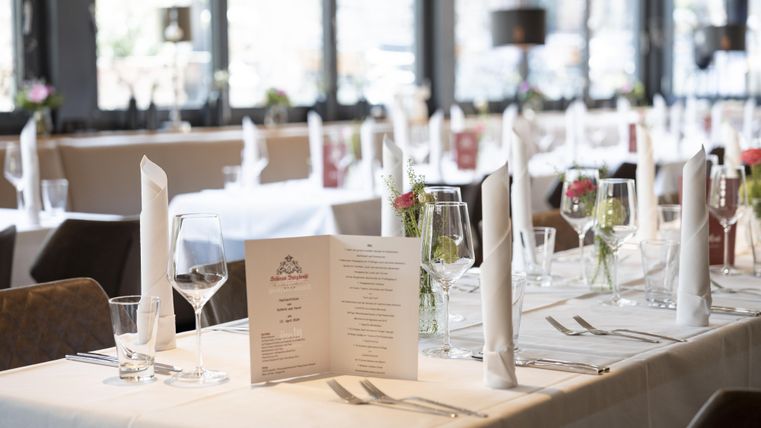 Ein elegantes Restaurant mit gedeckten Tischen und frischen Blumen. Die Menükarten sind sichtbar und das Licht sorgt für eine angenehme Atmosphäre.