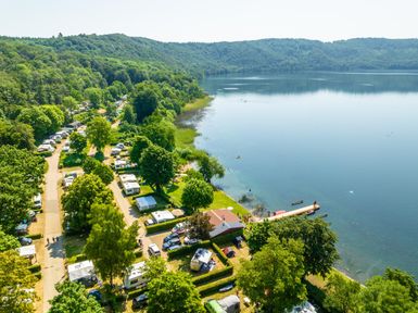 A picturesque landscape with a serene lake and surrounding trees. On the shore, there are campsites and a few boats visible.