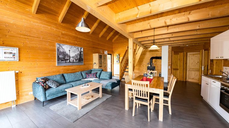 A cozy living area in a wooden house with a sofa and dining table. The wooden ceiling and walls create a warm atmosphere.