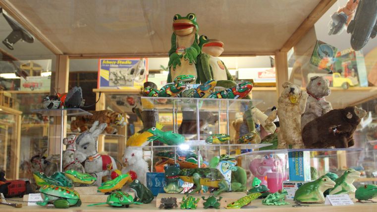 Eine Sammlung von Spielzeug, darunter Frösche, Hasen und andere Tiere, in einem Glaskasten. Die Figuren sind bunt und sorgsam angeordnet.