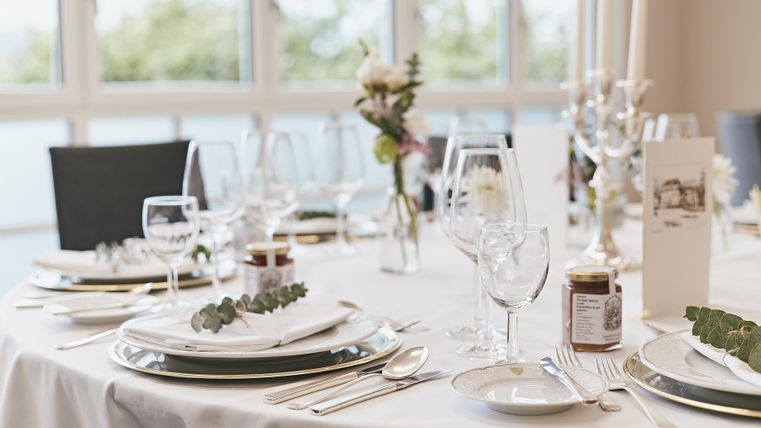 Ein stilvoll gedeckter Tisch mit eleganten Tellern, Gläsern und Besteck. Kleine Blumenarrangements und dekorative Elemente verleihen dem Ambiente eine festliche Note.