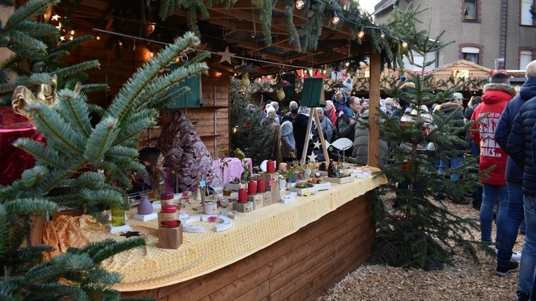 Ein stand auf einem Weihnachtsmarkt mit verschiedenen handgemachten Produkten. Im Hintergrund sind viele Besucher und Weihnachtsdekorationen zu sehen.