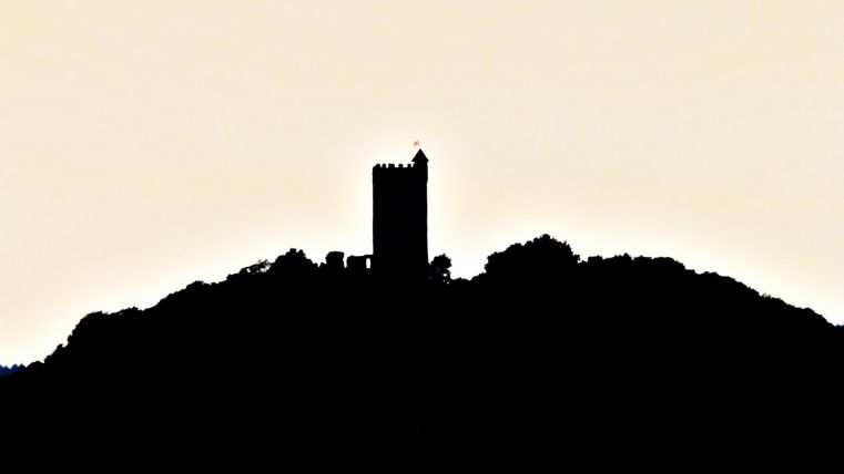 Ein markanter Turm steht auf einem Hügel vor einem hellen Hintergrund. Die Silhouette des Turms hebt sich deutlich ab.