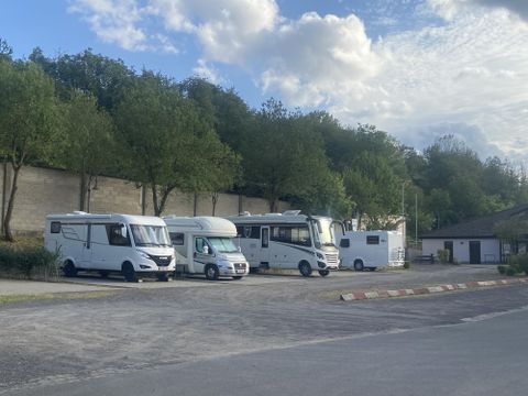 A parking lot with several motorhomes and trees in the background. The sky is partly cloudy and the surroundings appear calm.