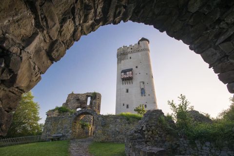 Eine alte Burgruine mit einem hohen Turm, umgeben von grüner Vegetation. Der Himmel ist klar und die Atmosphäre ist friedlich.