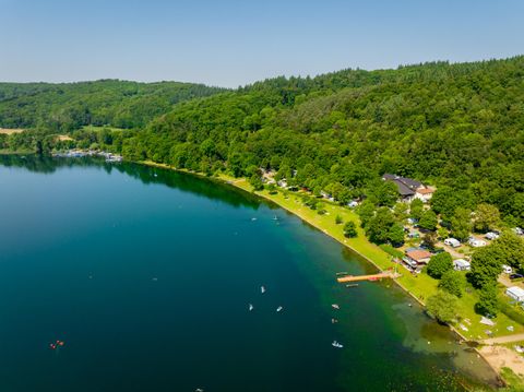 A tranquil lake surrounded by green forests. Some recreational activities and campsites can be seen along the shore.