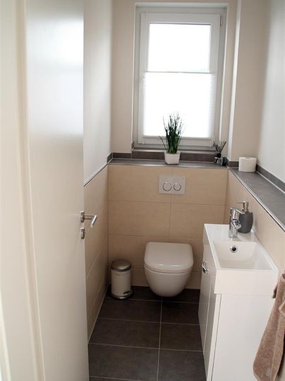 Ein modernes Badezimmer mit einer Toilette und einem kleinen Waschbecken. Große Fenster sorgen für viel Licht und eine angenehme Atmosphäre.