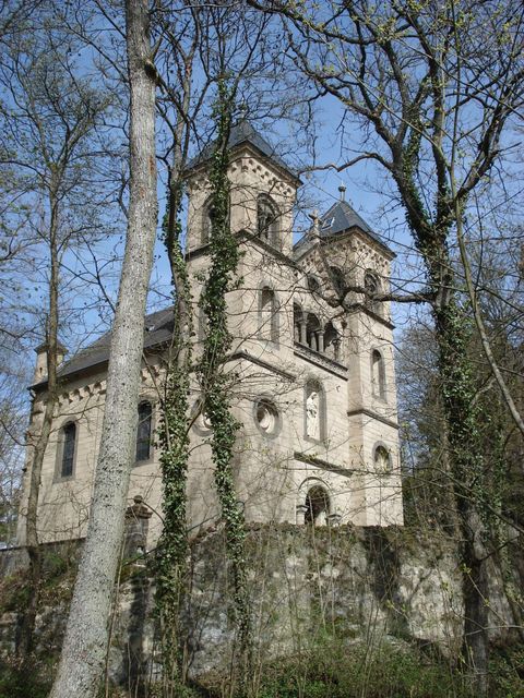 Eine alte Kirche, umgeben von Bäumen und Grün. Der Himmel ist blau und die Architektur ist markant.