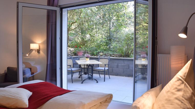 Ein gemütliches Schlafzimmer mit Blick auf eine Terrasse. Die offene Tür lässt viel Licht und einen Blick auf den grünen Garten zu.
