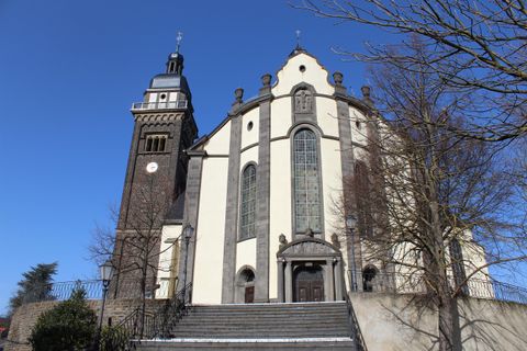 Eine beeindruckende Kirche mit einem hohen Turm und großen Fenstern. Der blaue Himmel und die Bäume im Vordergrund verleihen dem Bild eine ruhige Atmosphäre.