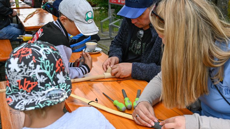 A group of people is working together on a craft project. They are using tools and materials on a table outdoors.
