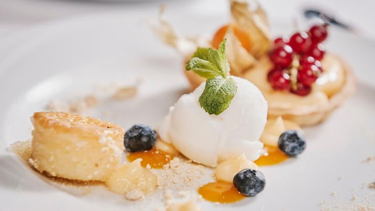 Ein köstliches Dessertgericht mit einer Kugel Eis, frischen Beeren und einer süßen Tarte. Das Gericht ist elegant angerichtet und wirkt sehr ansprechend.