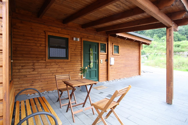 Eine gemütliche Holzveranda mit einem Tisch und Stühlen. Die Umgebung ist grün und einladend.