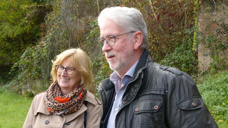 Een vrolijk paar staat buiten. Op de achtergrond zijn planten en bomen te zien.