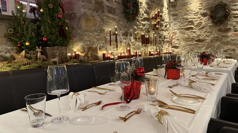 Ein festlich gedeckter Tisch in einem gemütlichen Restaurant. Die Dekoration umfasst Weihnachtsbaumzweige, Kerzen und rote Akzente.