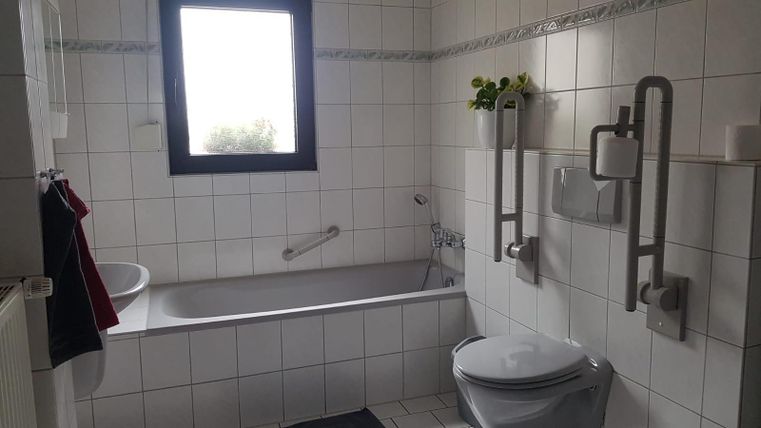 A modern bathroom with a bathtub, a sink, and a toilet. The walls are tiled, and a window provides daylight.