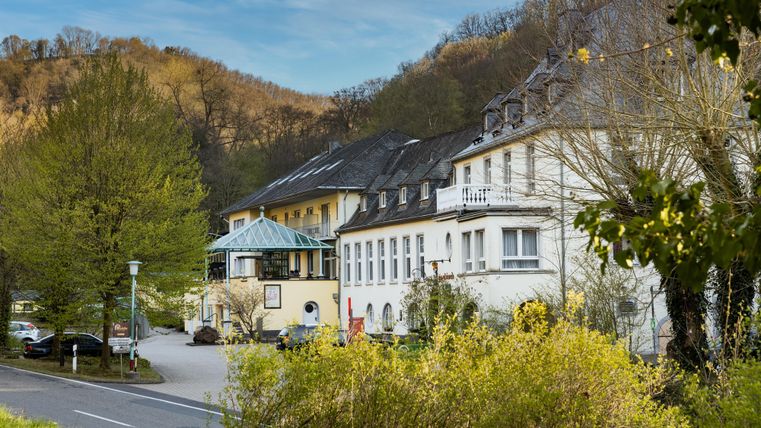 Ein malerisches Gebäude inmitten von Bäumen und Hügeln. Die Umgebung ist grün und einladend.